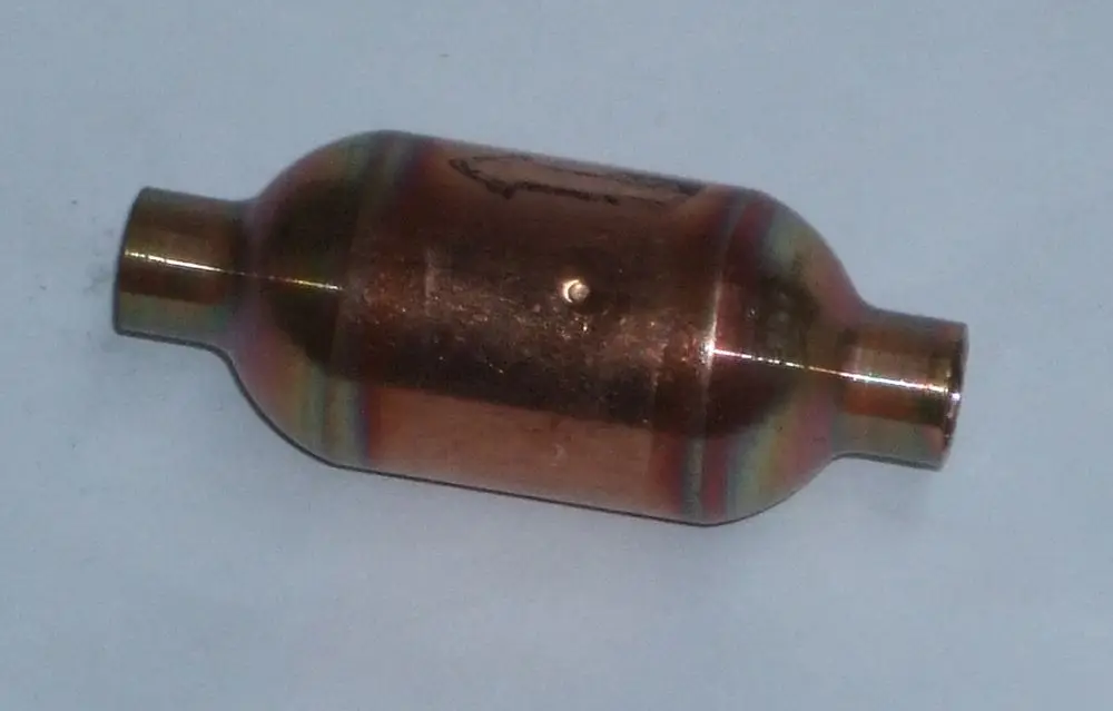 Metallischer Schalldämpfer mit runder Form und zwei Anschlüssen. Produkt von Daikin, verwendet zur Geräuschreduzierung in Heizsystemen.